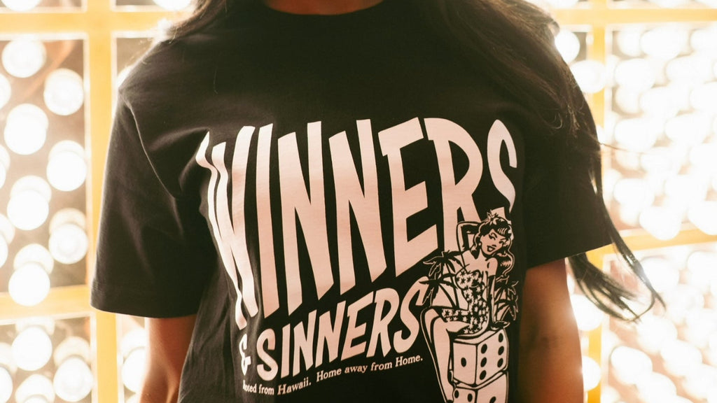 Woman wearing a black t-shirt with 'Winners & Sinners' text and graphic design.